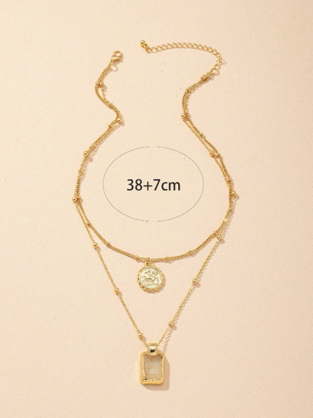 Gold layered necklace with two pendants on a beige background