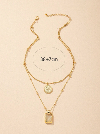 Gold layered necklace with two pendants on a beige background
