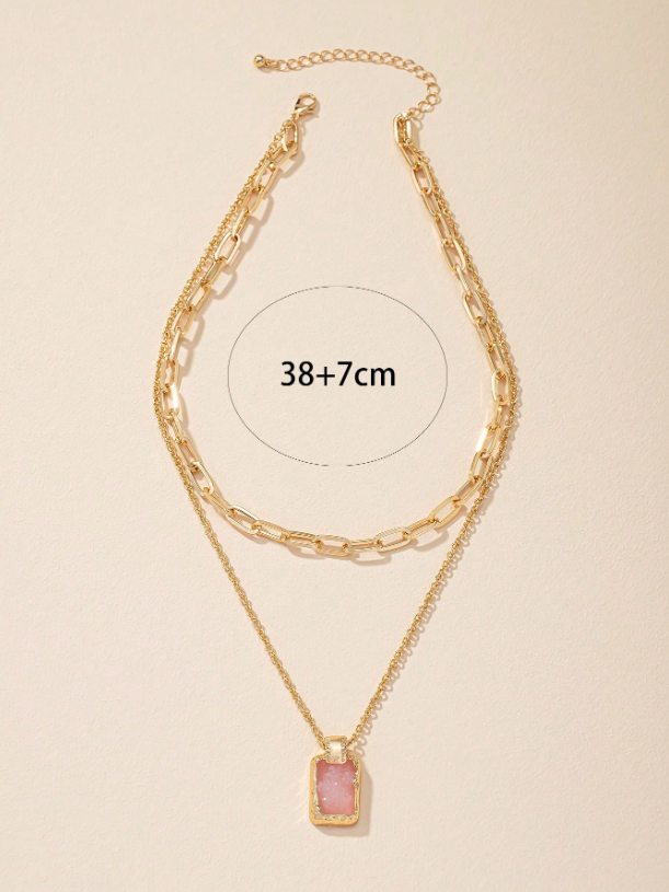 Gold chain necklace with a pink pendant on a beige background