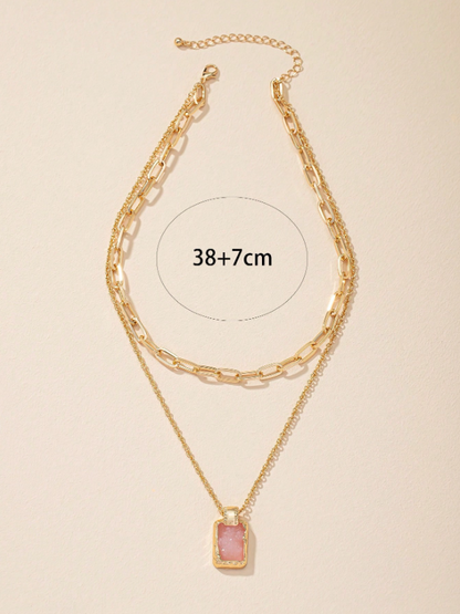 Gold chain necklace with a pink pendant on a beige background