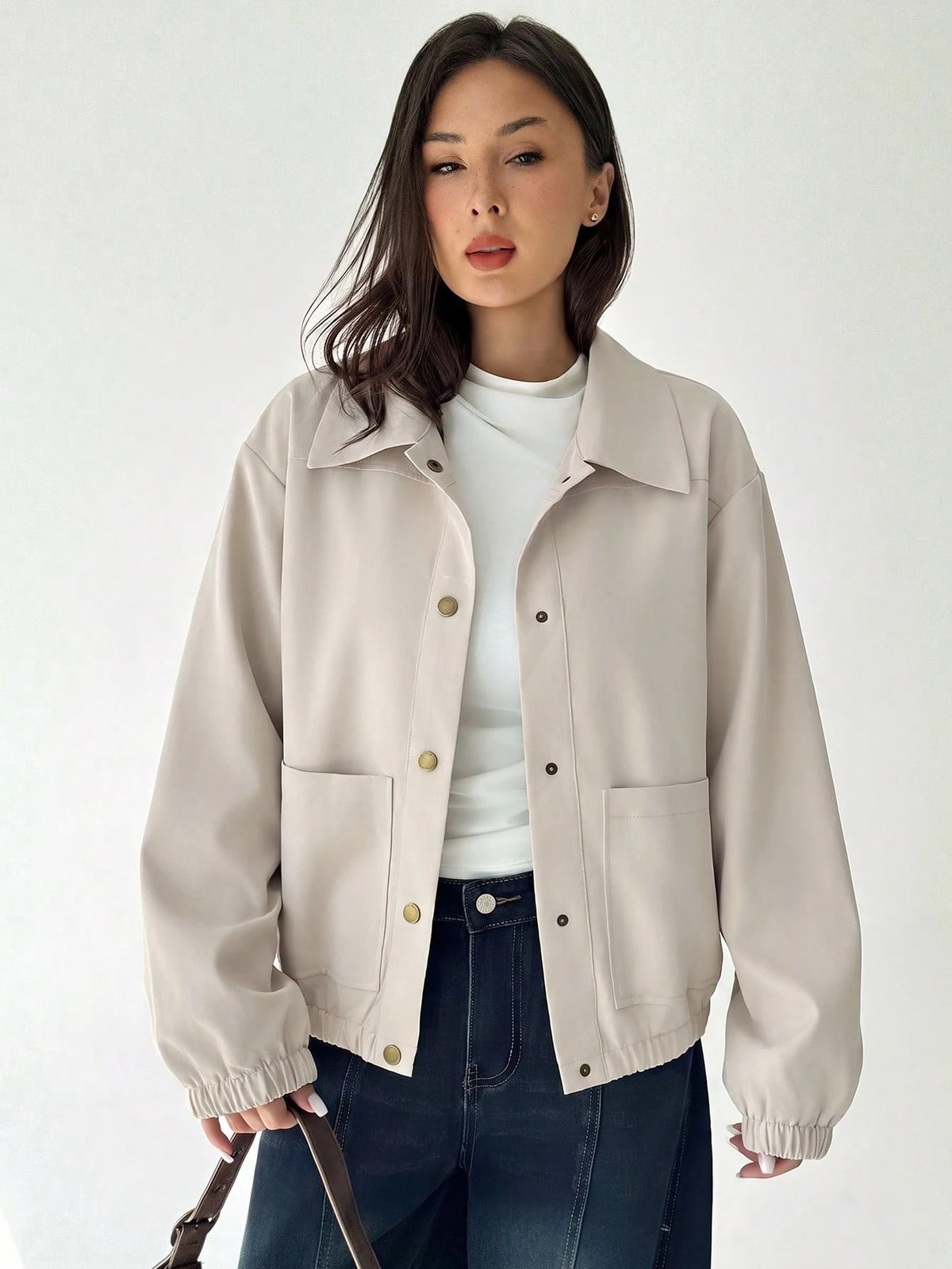A woman wearing a Beige casual jacket with a contrasting brown lapel collar, drop shoulders, and front pockets paired with a white tee and dark jeans