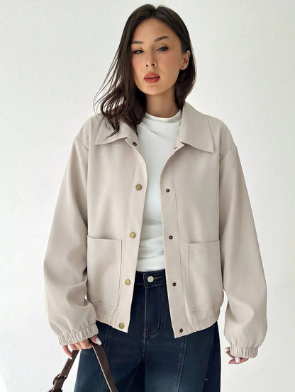 A woman wearing a Beige casual jacket with a contrasting brown lapel collar, drop shoulders, and front pockets paired with a white tee and dark jeans