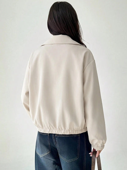 A woman wearing a Beige casual jacket with a contrasting brown lapel collar, drop shoulders, and front pockets paired with a white tee and dark jeans