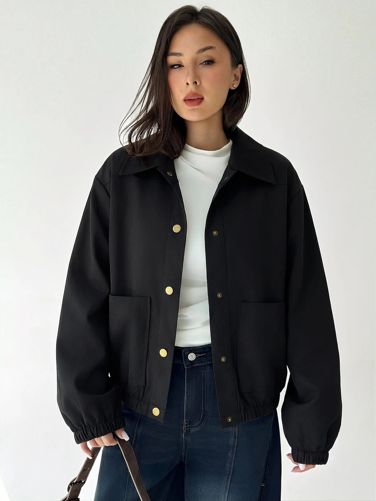 A woman wearing a Black casual jacket with a contrasting brown lapel collar, drop shoulders, and front pockets paired with a white tee and dark jeans