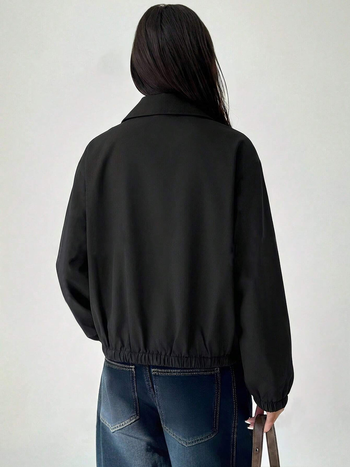 A woman wearing a Black casual jacket with a contrasting brown lapel collar, drop shoulders, and front pockets paired with a white tee and dark jeans