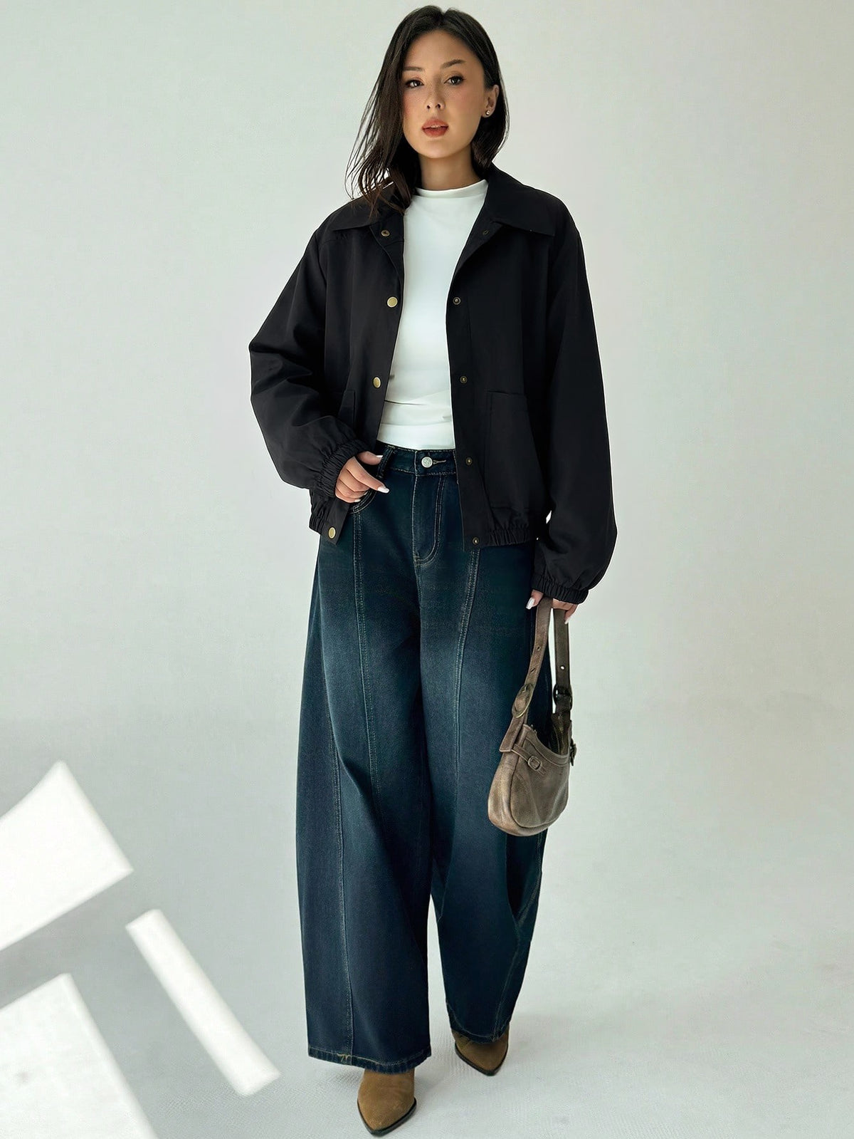 A woman wearing a Black casual jacket with a contrasting brown lapel collar, drop shoulders, and front pockets paired with a white tee and dark jeans