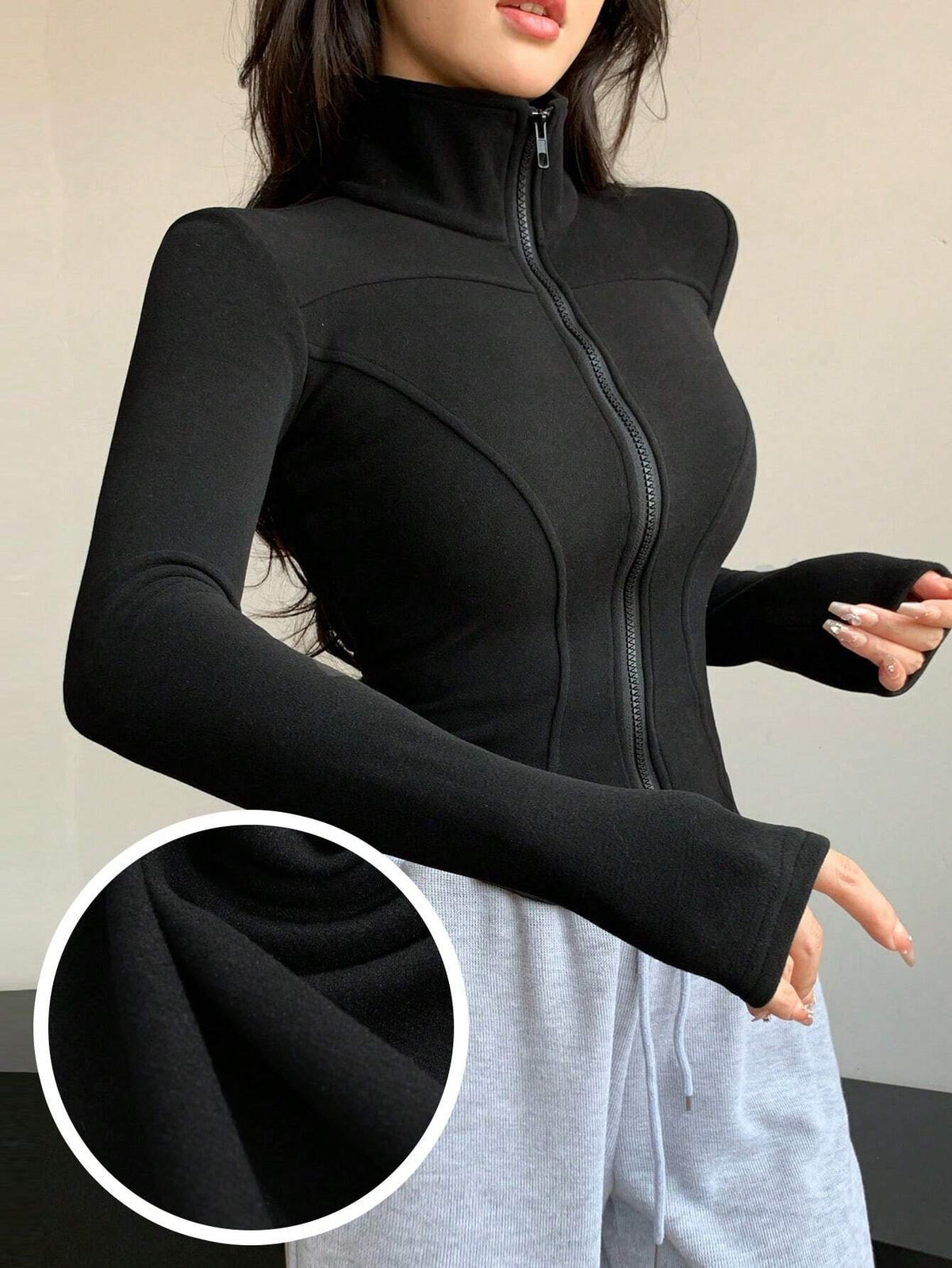 A woman wearing a black ribbed trim zip-up sweatshirt jacket with a high mock neck paired with light grey sweatpants
