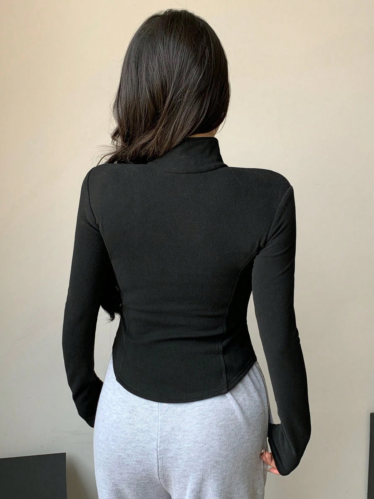 A woman wearing a black ribbed trim zip-up sweatshirt jacket with a high mock neck paired with light grey sweatpants
