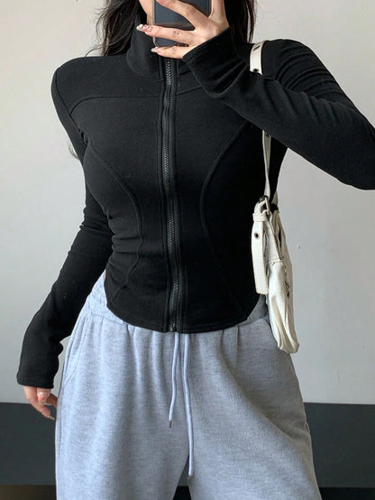 A woman wearing a black ribbed trim zip-up sweatshirt jacket with a high mock neck paired with light grey sweatpants