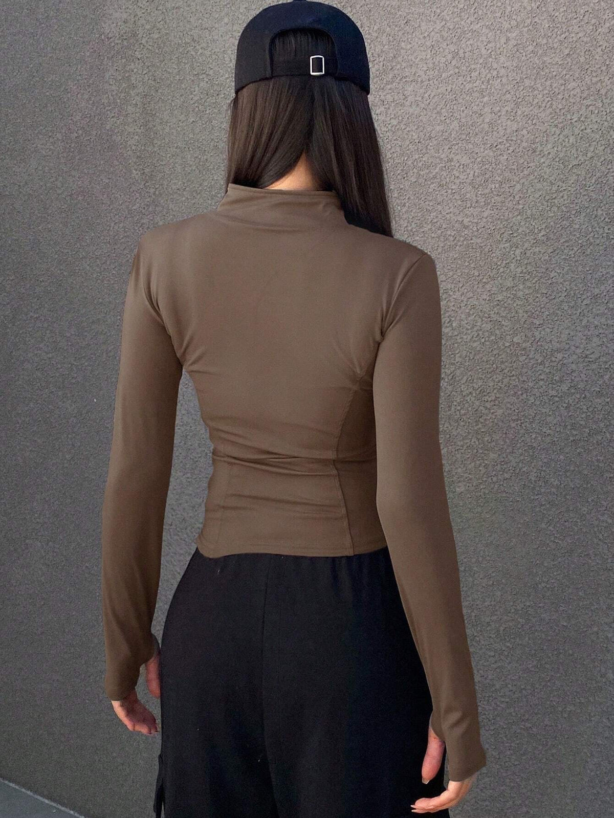 A woman wearing a brown long-sleeve zip-up jacket with thumb holes and a high mock neck paired with black pants