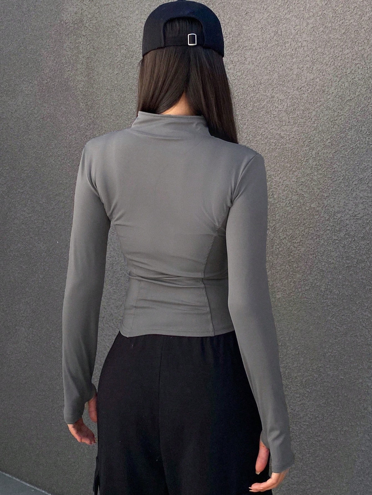 A woman wearing a grey long-sleeve zip-up jacket with thumb holes and a high mock neck paired with black pants