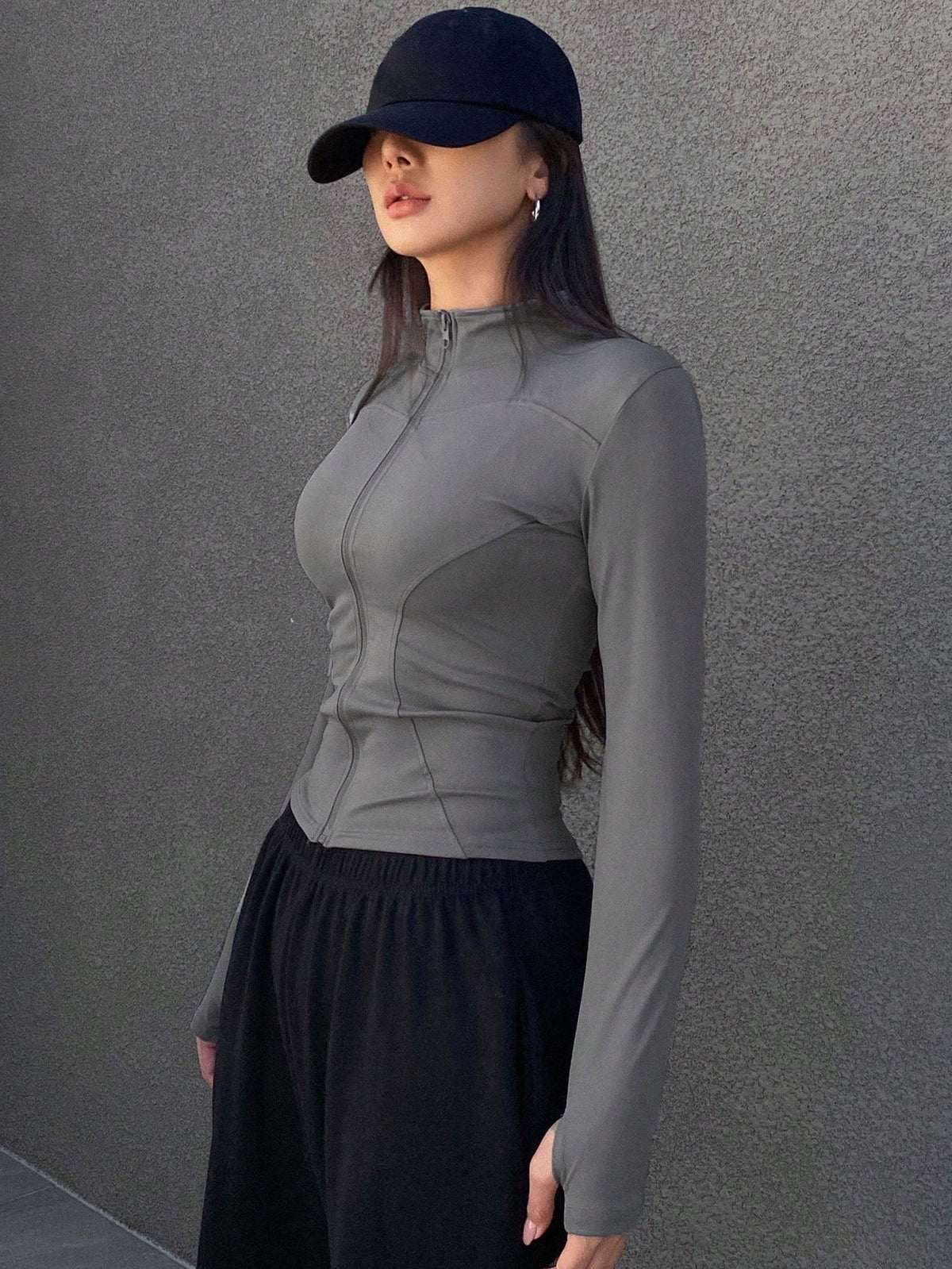 A woman wearing a grey long-sleeve zip-up jacket with thumb holes and a high mock neck paired with black pants