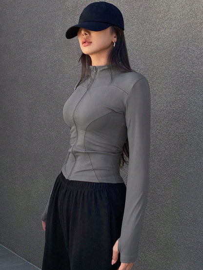 A woman wearing a grey long-sleeve zip-up jacket with thumb holes and a high mock neck paired with black pants
