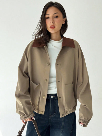 A woman wearing a khaki casual jacket with a contrasting brown lapel collar, drop shoulders, and front pockets paired with a white tee and dark jeans