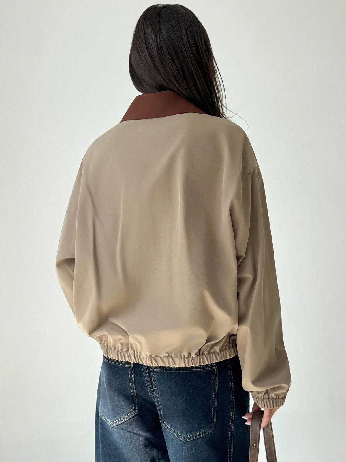 A woman wearing a khaki casual jacket with a contrasting brown lapel collar, drop shoulders, and front pockets paired with a white tee and dark jeans