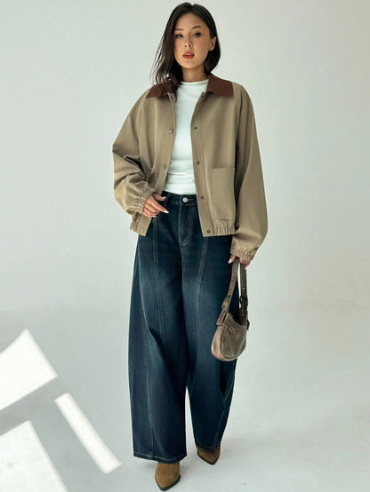 A woman wearing a khaki casual jacket with a contrasting brown lapel collar, drop shoulders, and front pockets paired with a white tee and dark jeans