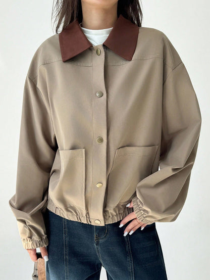 A woman wearing a khaki casual jacket with a contrasting brown lapel collar, drop shoulders, and front pockets paired with a white tee and dark jeans