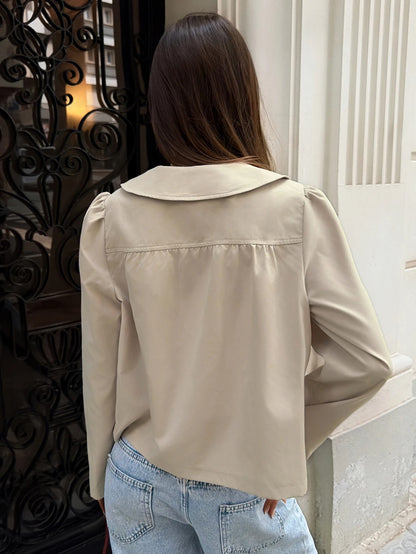 A woman wearing a khaki short trench jacket with a Peter Pan collar and tortoiseshell buttons paired with a white top and black pants