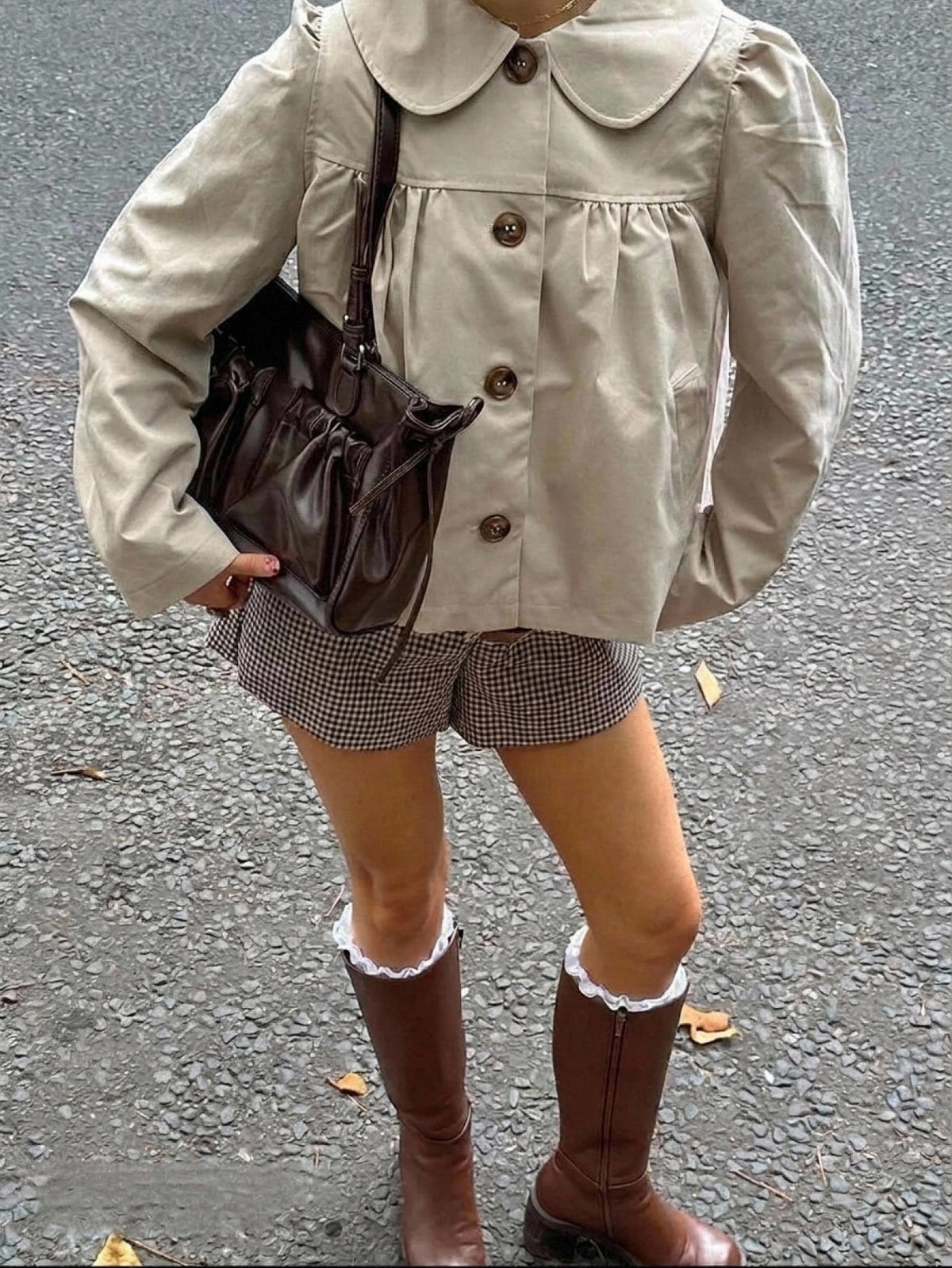A woman wearing a khaki short trench jacket with a Peter Pan collar and tortoiseshell buttons paired with a white top and black pants