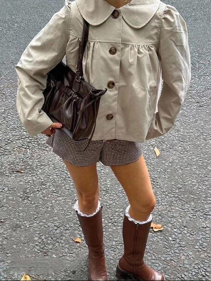 A woman wearing a khaki short trench jacket with a Peter Pan collar and tortoiseshell buttons paired with a white top and black pants