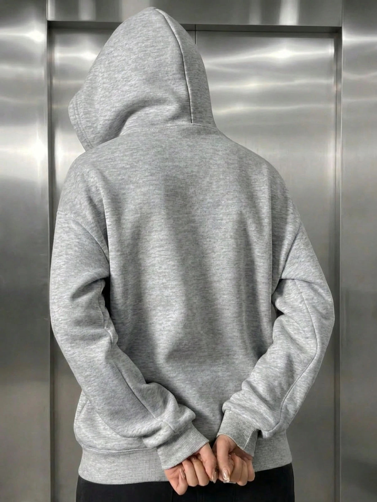A woman wearing a light grey fleece balaclava zip-up hoodie featuring an integrated face mask and front pockets while standing indoors