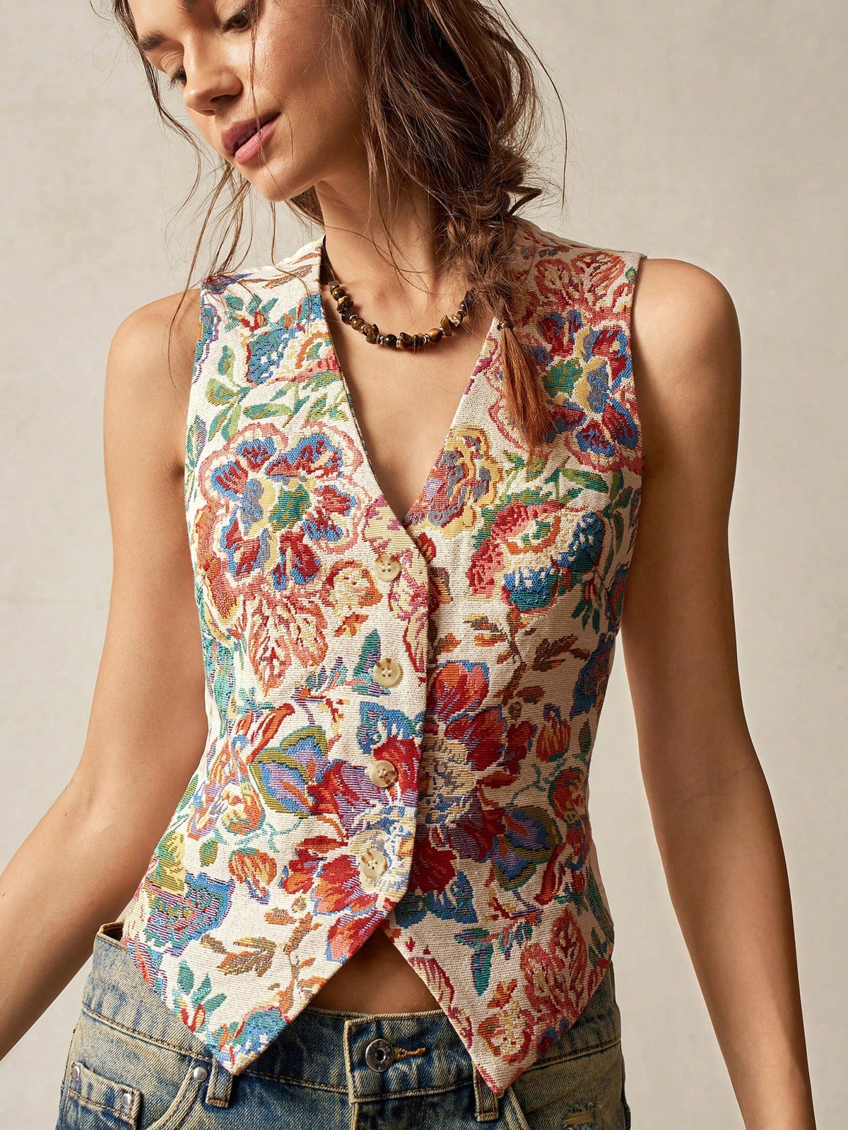 A woman wearing a multicolor floral jacquard boho vest with a V-neck and button closure paired with denim jeans