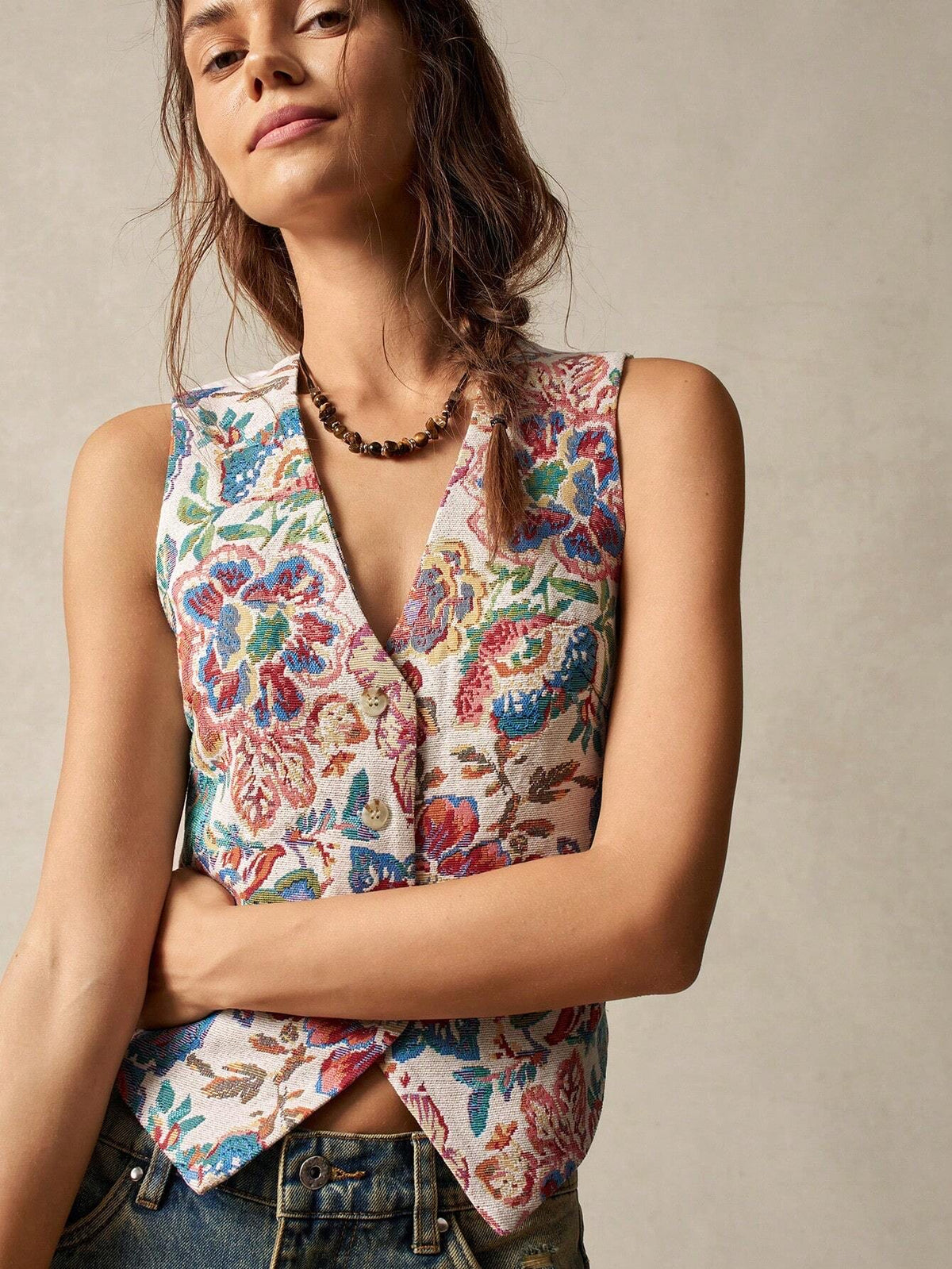 A woman wearing a multicolor floral jacquard boho vest with a V-neck and button closure paired with denim jeans