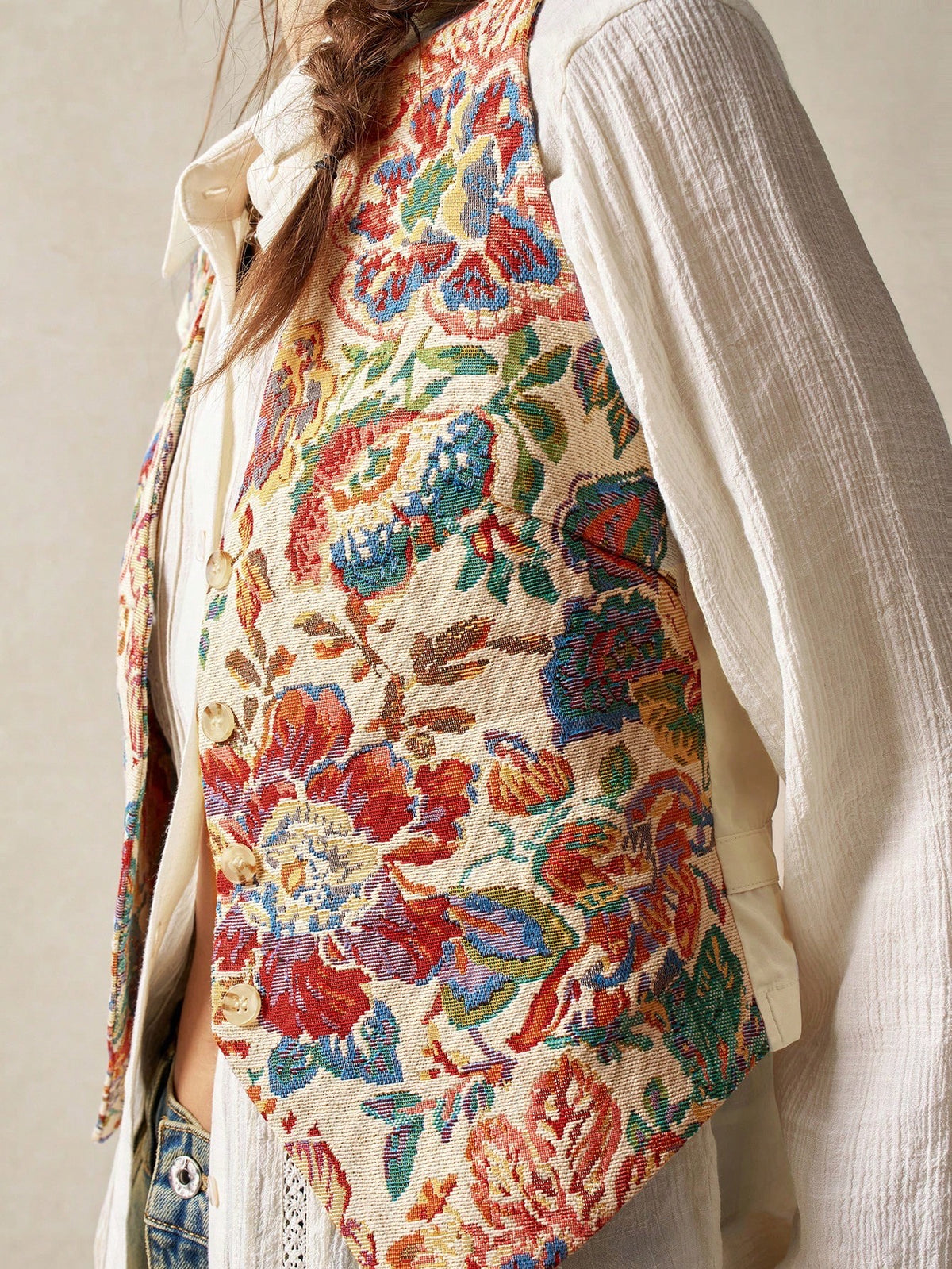 A woman wearing a multicolor floral jacquard boho vest with a V-neck and button closure paired with denim jeans