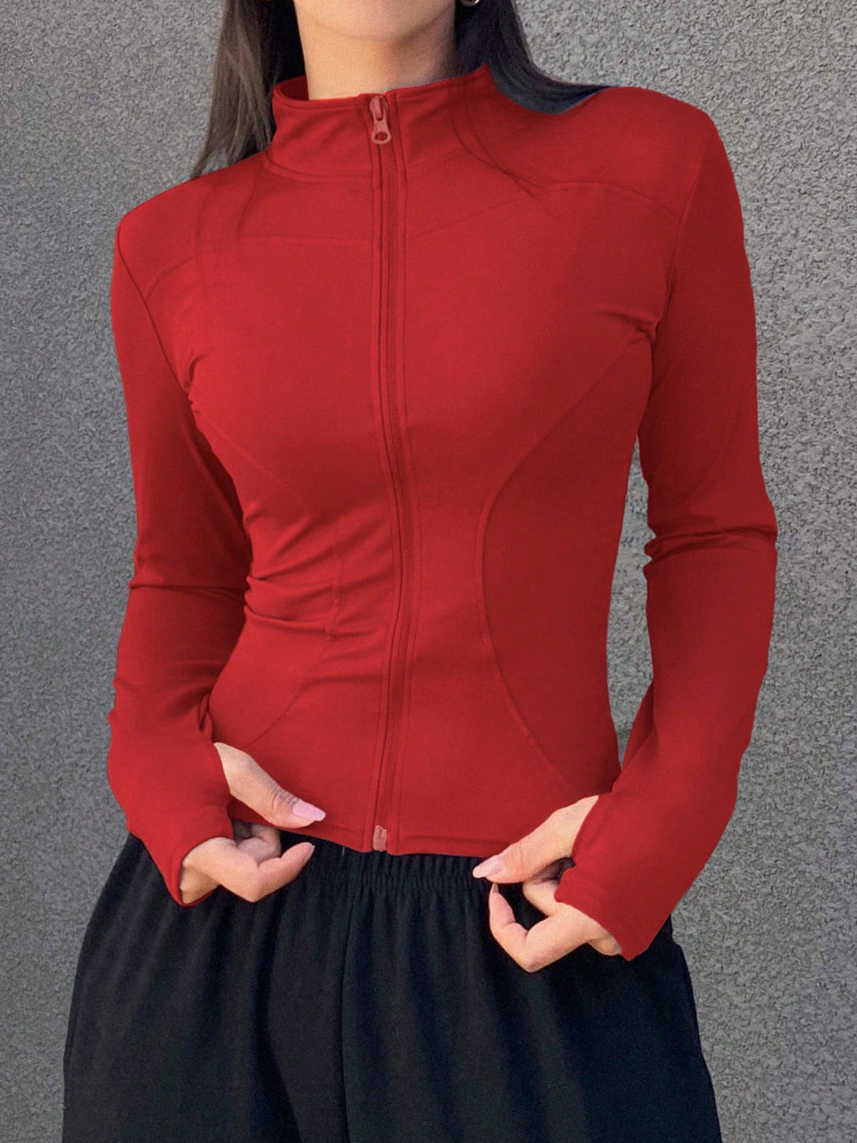 A woman wearing a red long-sleeve zip-up jacket with thumb holes and a high mock neck paired with black pants