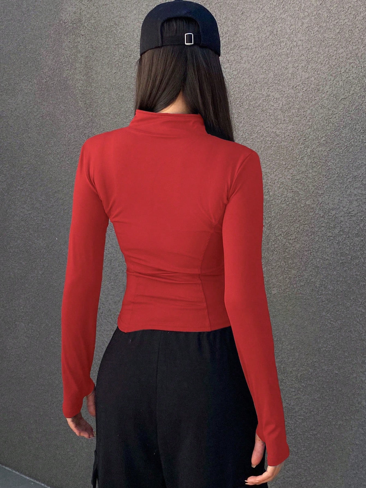 A woman wearing a red long-sleeve zip-up jacket with thumb holes and a high mock neck paired with black pants