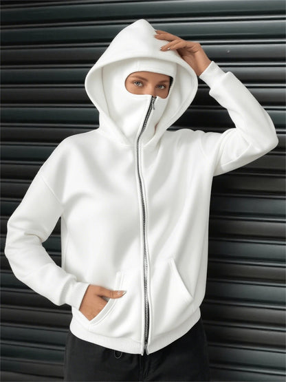 A woman wearing a white fleece balaclava zip-up hoodie featuring an integrated face mask and front pockets while standing indoors