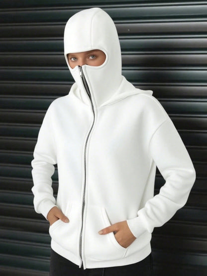 A woman wearing a white fleece balaclava zip-up hoodie featuring an integrated face mask and front pockets while standing indoors