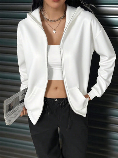 A woman wearing a white fleece balaclava zip-up hoodie featuring an integrated face mask and front pockets while standing indoors