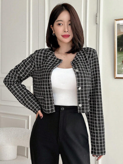 A woman wearing an Black plaid tweed crop jacket featuring a round neckline and long sleeves paired with a pleated skirt