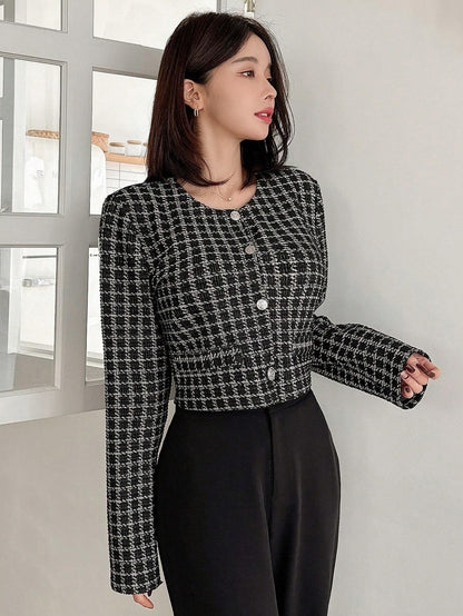 A woman wearing an Black plaid tweed crop jacket featuring a round neckline and long sleeves paired with a pleated skirt