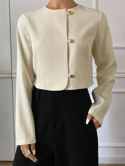 A woman wearing an apricot short jacket featuring gold button accents and long sleeves paired with high-waisted black trousers