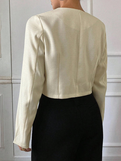 A woman wearing an apricot short jacket featuring gold button accents and long sleeves paired with high-waisted black trousers