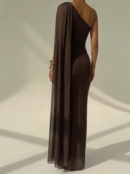 A woman wearing an elegant coffee brown one-shoulder ruched mermaid long dress with a dramatic flutter cloak sleeve