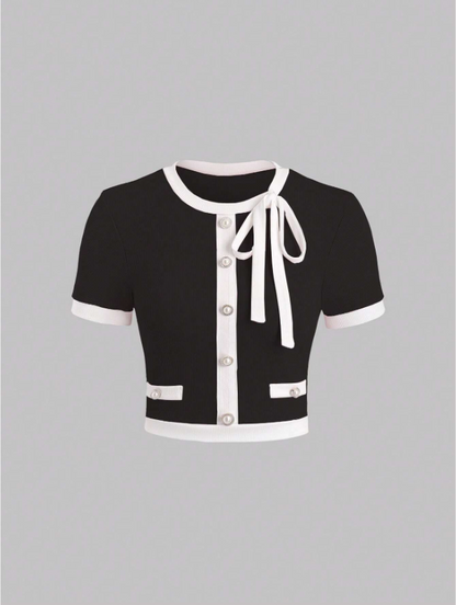 Black cardigan with white trim and bow on a gray background
