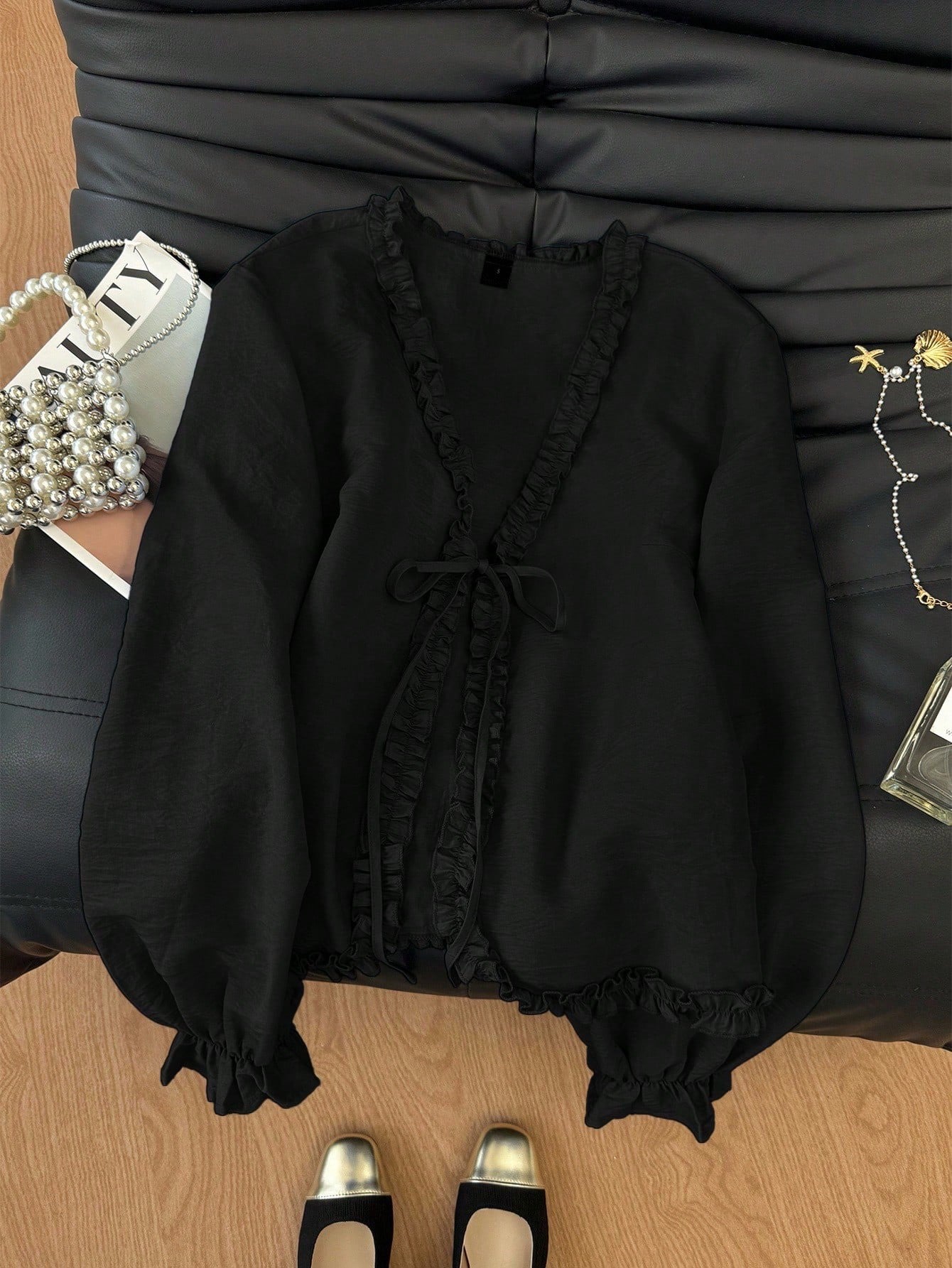 Black frill trim tie-front long-sleeve blouse with delicate ruffles laid flat on a dark textured background