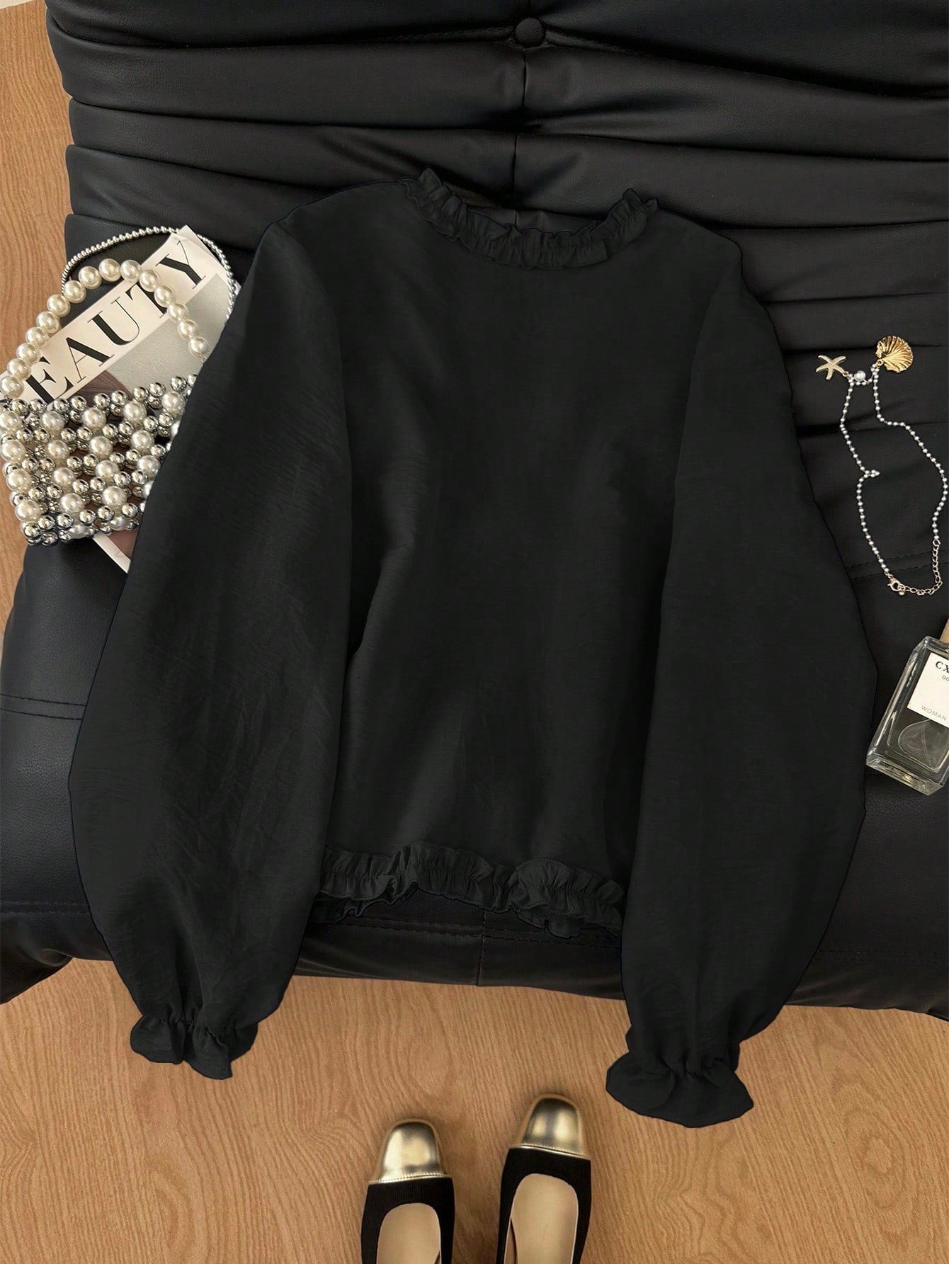 Black frill trim tie-front long-sleeve blouse with delicate ruffles laid flat on a dark textured background