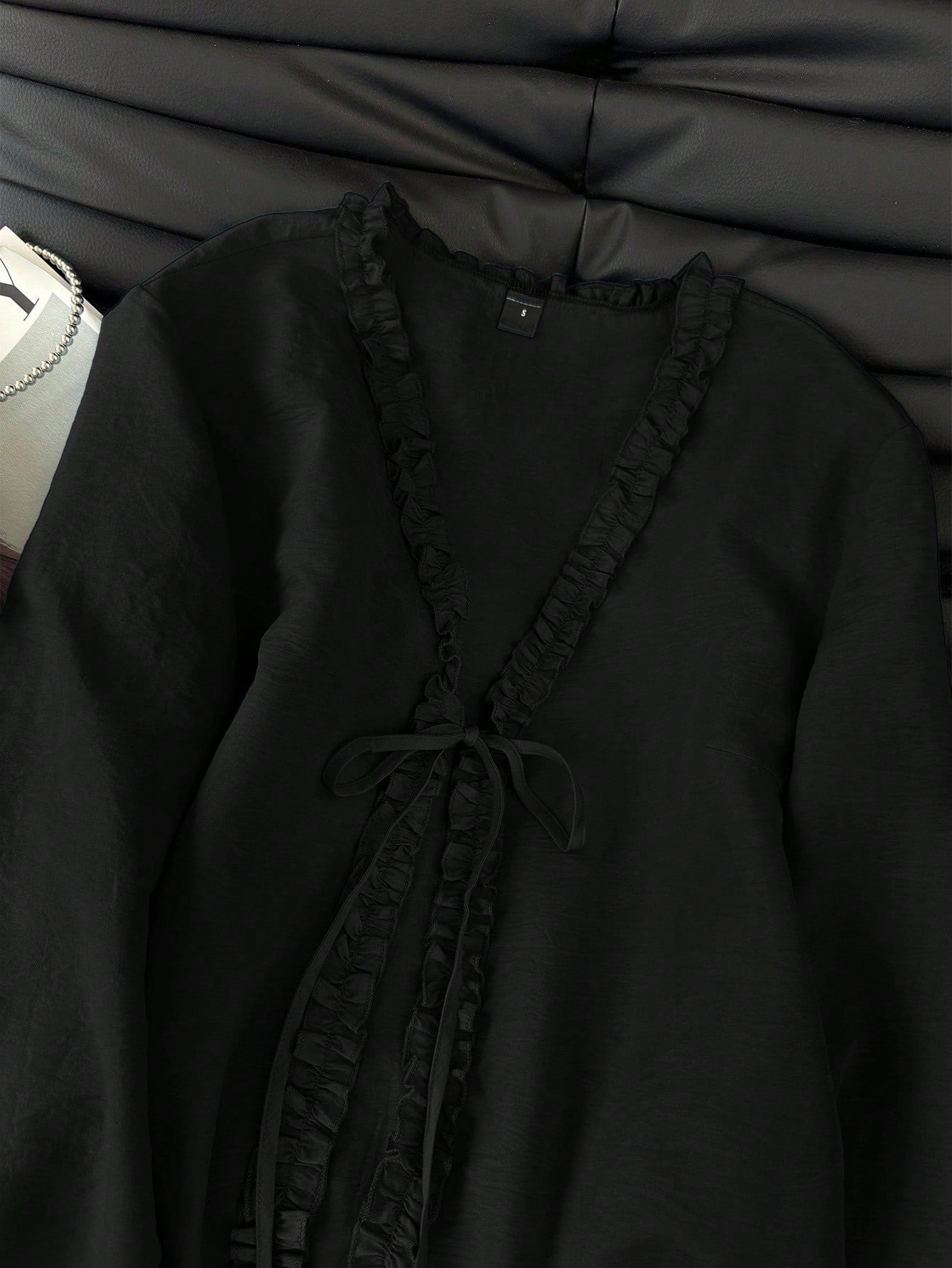 Black frill trim tie-front long-sleeve blouse with delicate ruffles laid flat on a dark textured background