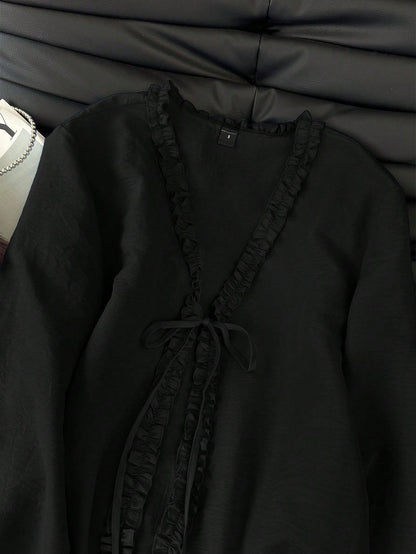 Black frill trim tie-front long-sleeve blouse with delicate ruffles laid flat on a dark textured background