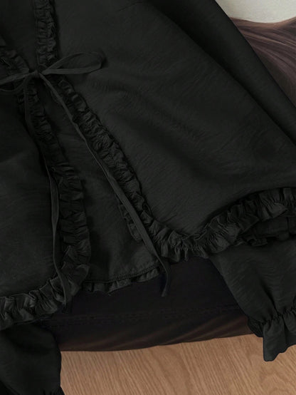 Black frill trim tie-front long-sleeve blouse with delicate ruffles laid flat on a dark textured background
