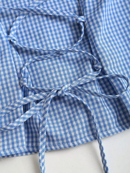 Blue and white gingham plaid short-sleeve polo collar peplum blouse with front ruffles and a laced-up back detail laid flat