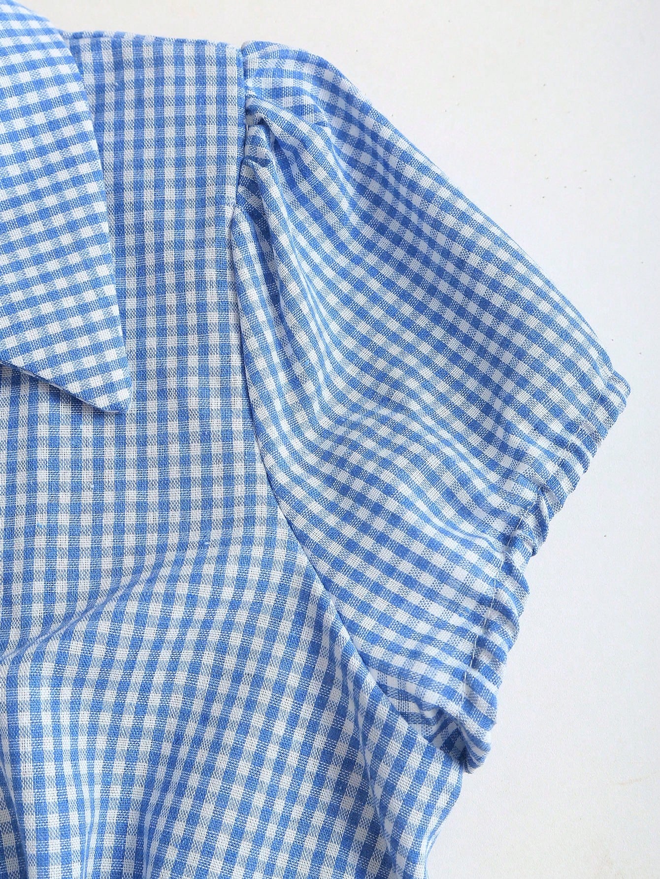 Blue and white gingham plaid short-sleeve polo collar peplum blouse with front ruffles and a laced-up back detail laid flat