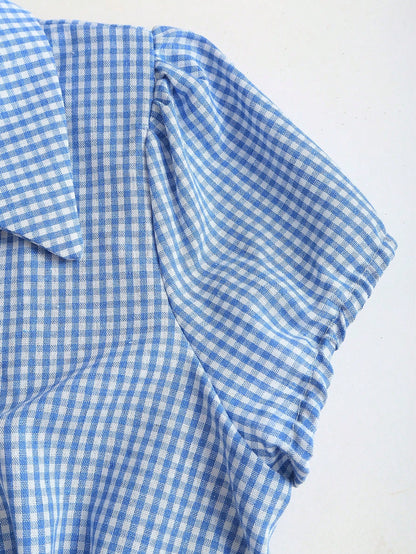 Blue and white gingham plaid short-sleeve polo collar peplum blouse with front ruffles and a laced-up back detail laid flat