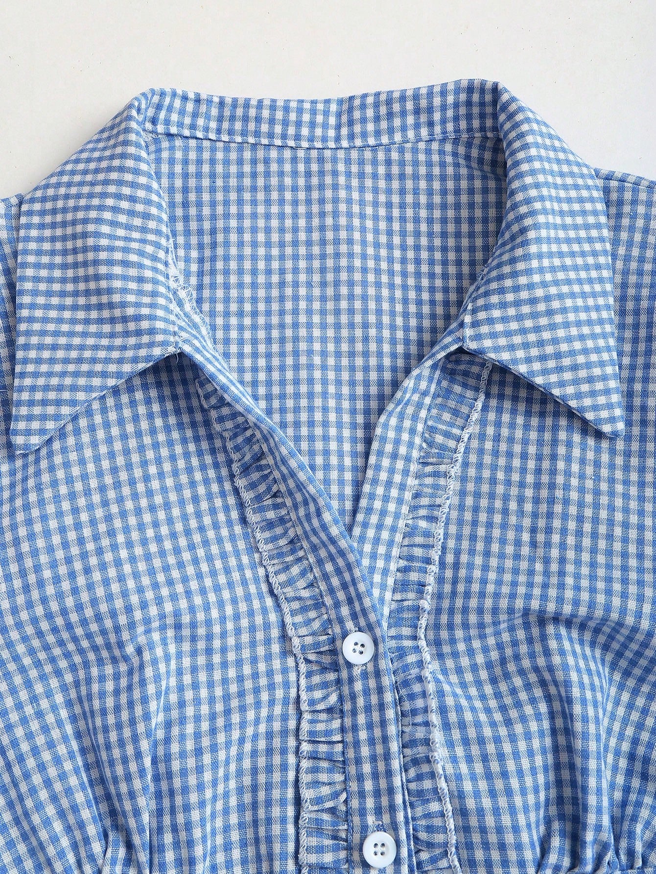 Blue and white gingham plaid short-sleeve polo collar peplum blouse with front ruffles and a laced-up back detail laid flat
