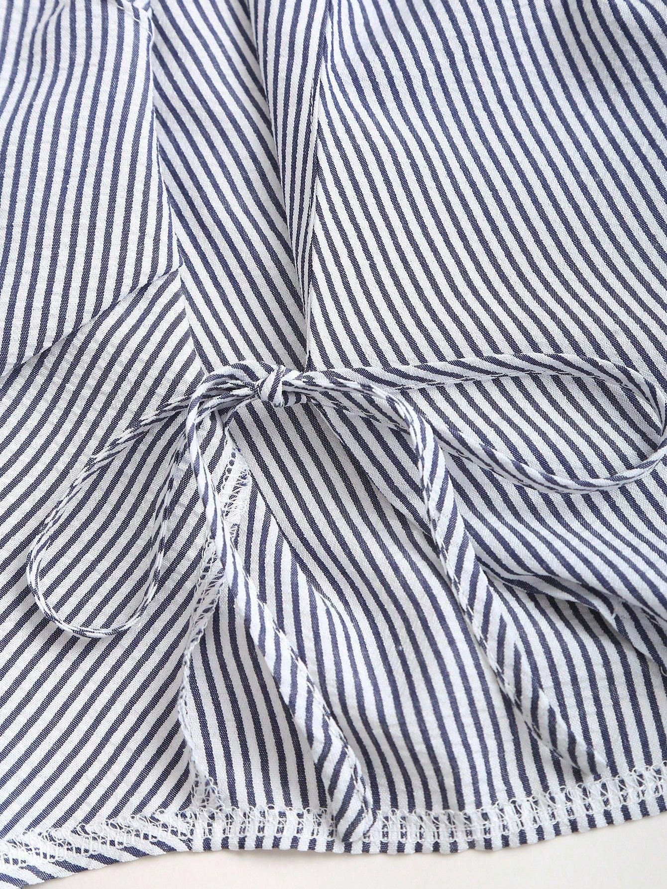 Blue and white striped wrap blouse with a collar, waist bow tie, and long flare sleeves laid flat against a neutral background