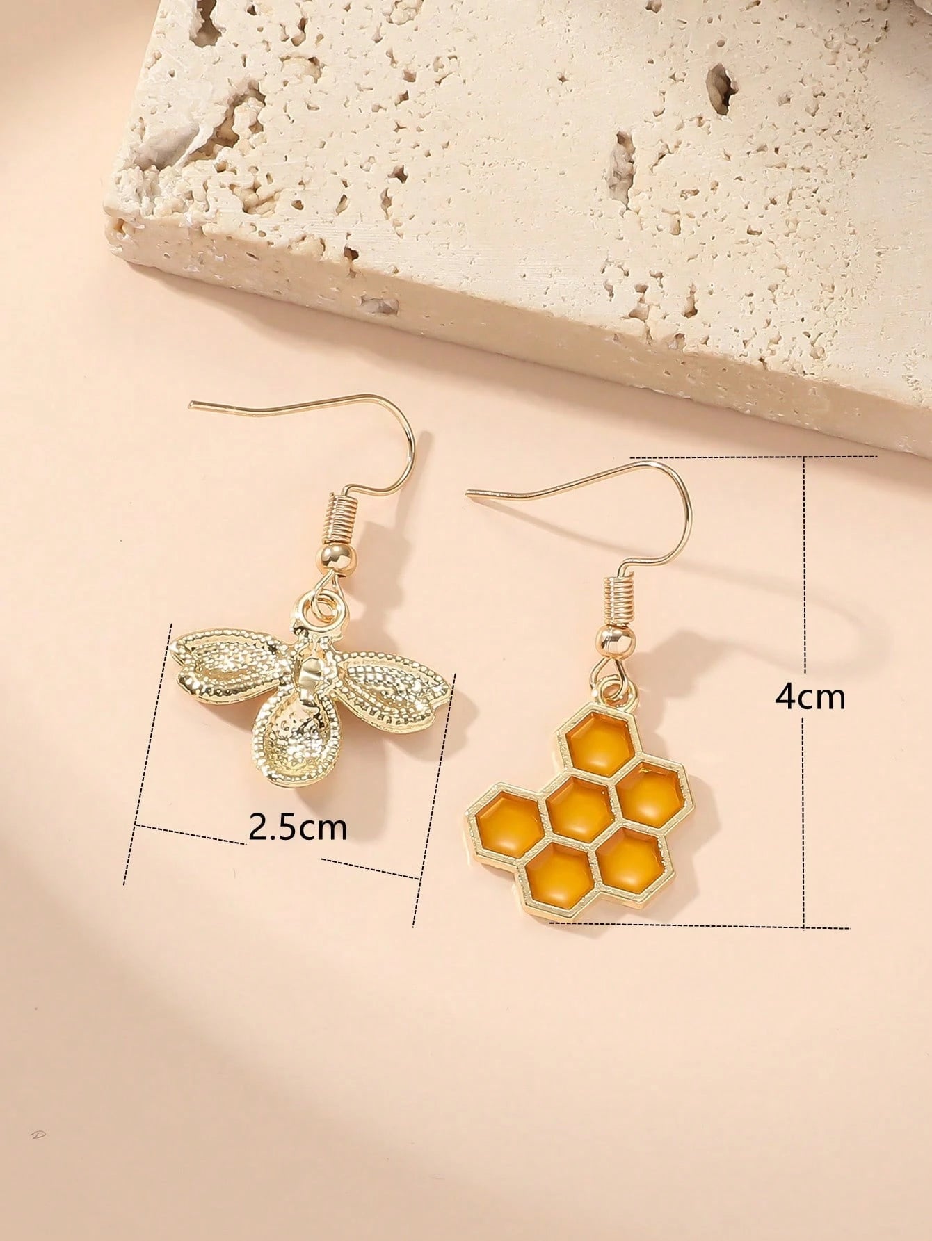 Two pairs of earrings with bee and honeycomb designs on a beige background.